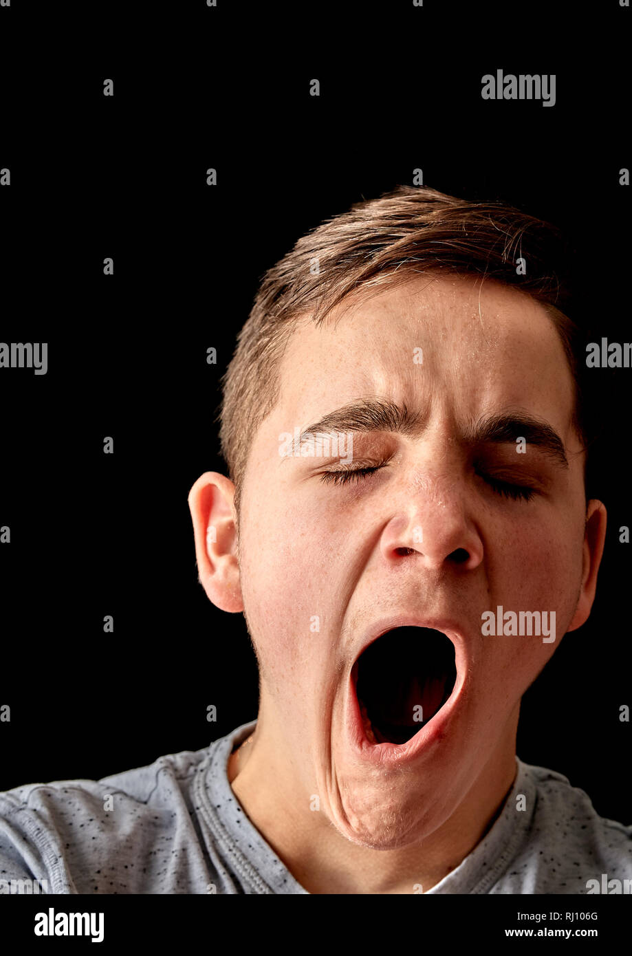 Un annoiato adolescente maschio sbadigli con la bocca aperta Foto Stock