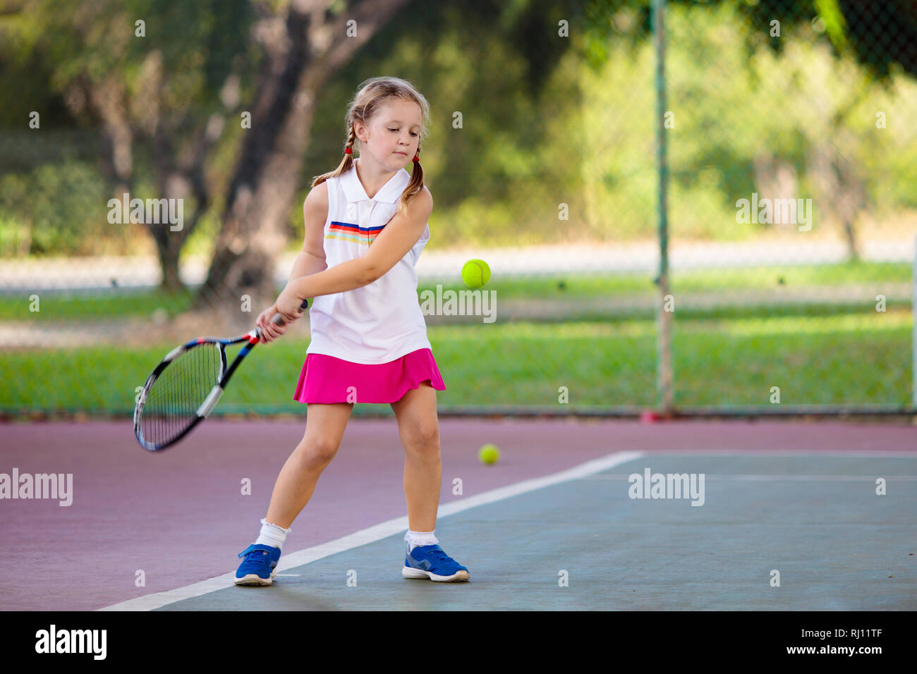 Bambino gioca a tennis sulla corte interna. Bambina con la racchetta e la palla in sport club. Esercizio attivo per i bambini. Attività estive per bambini. Foto Stock