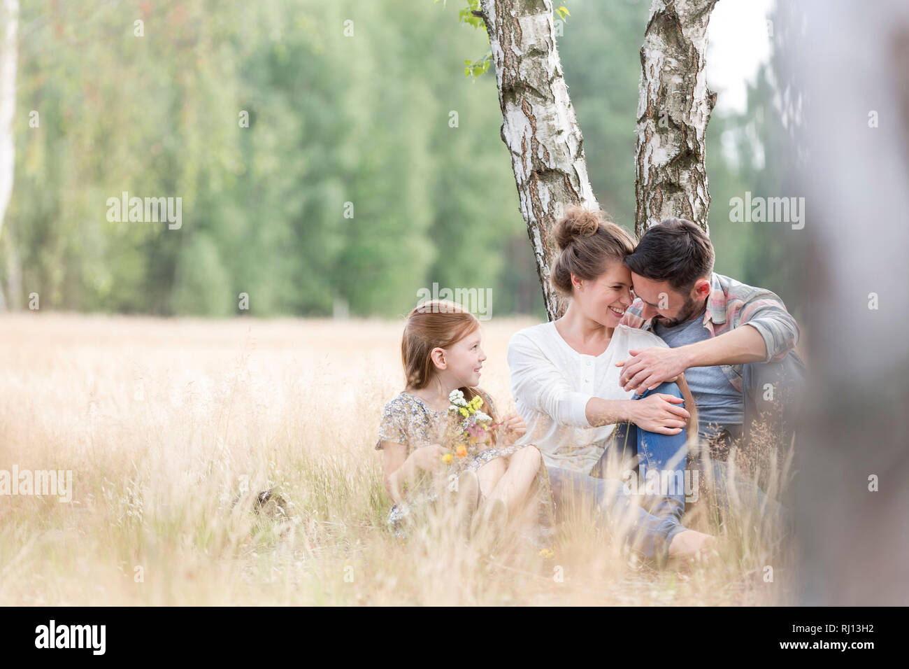 Figlia cercando di amare i genitori mentre è seduto sul campo in terreni agricoli Foto Stock