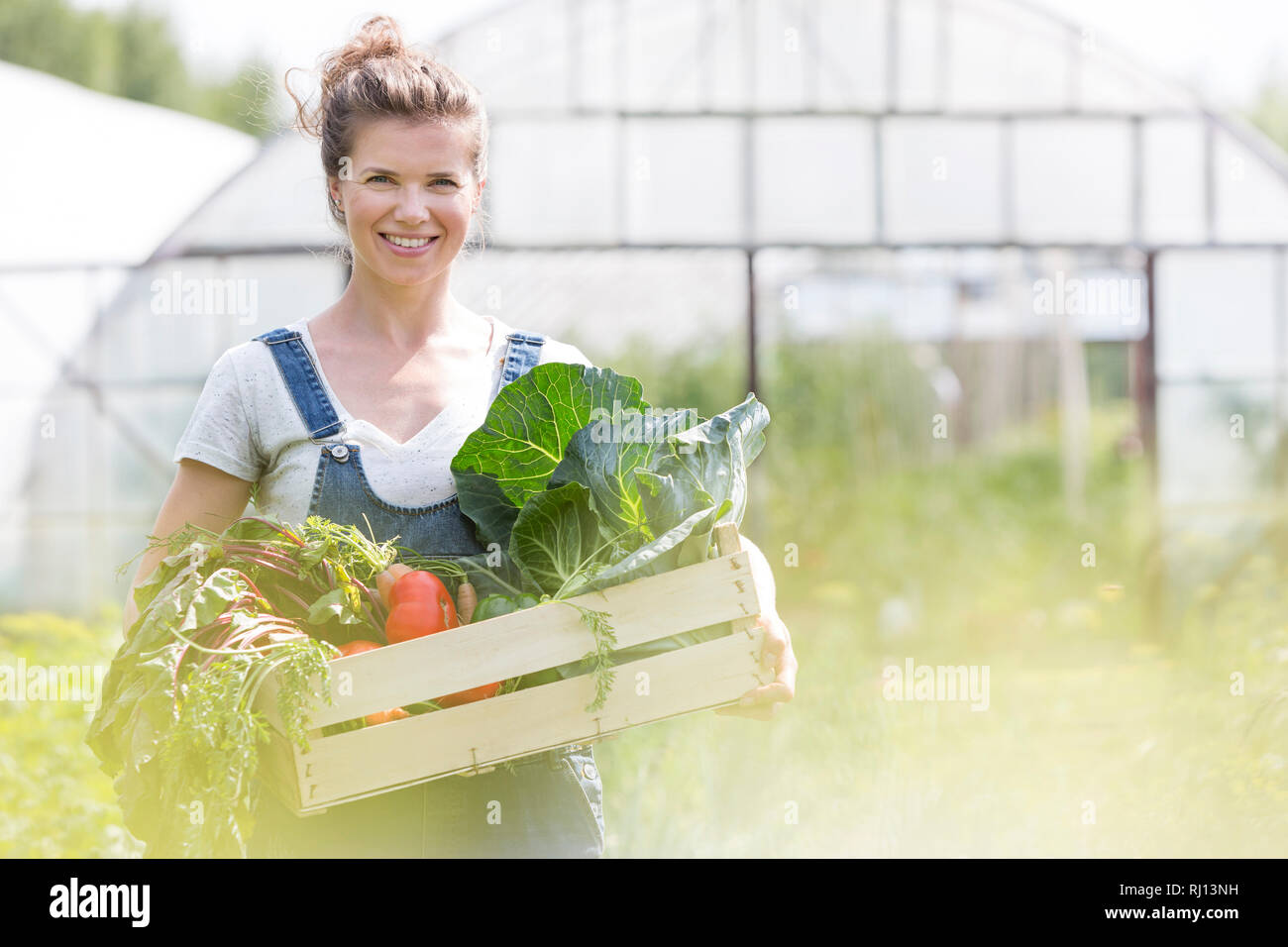 Ritratto di donna sorridente tenendo le verdure in cassa presso l'azienda Foto Stock