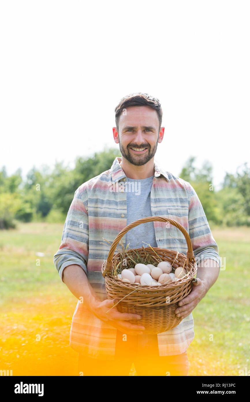 Sorridente metà adulto l'agricoltore che detiene le uova nel paniere a livello di azienda Foto Stock