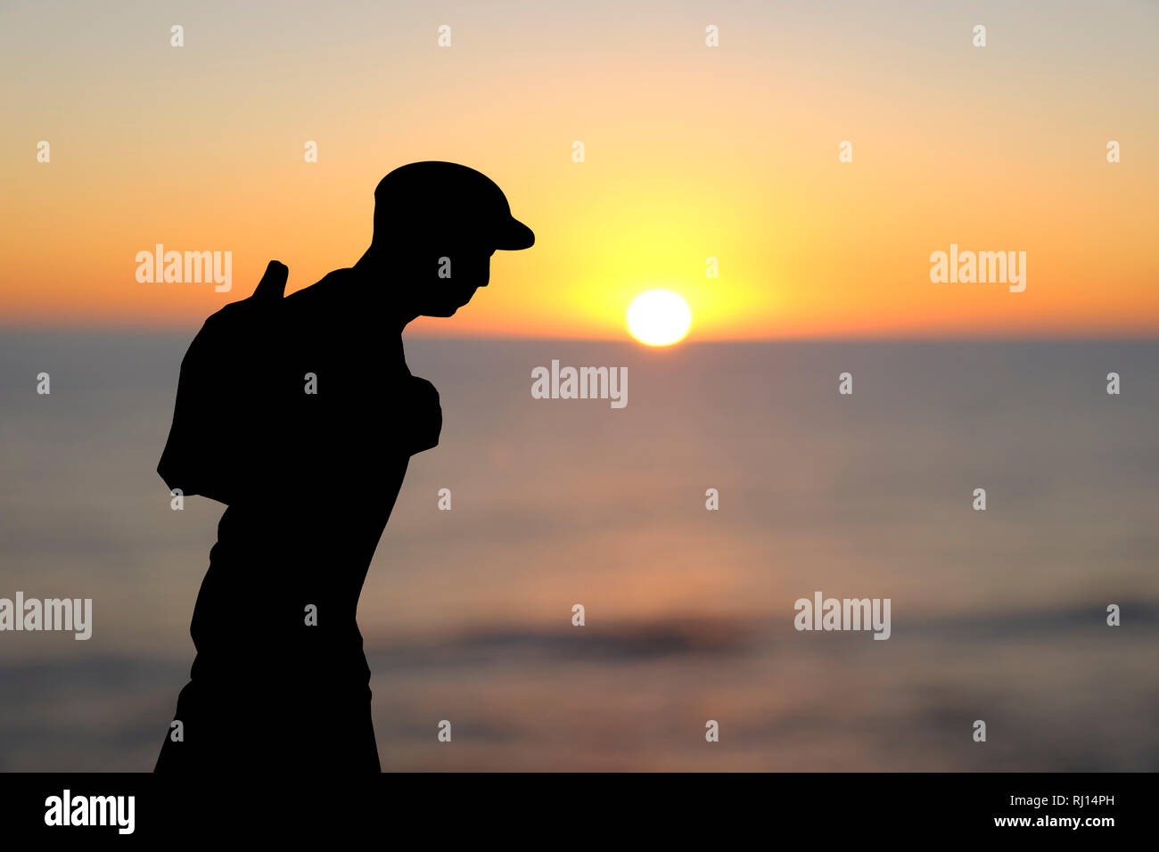 Primo piano di un ritaglio di carta nella forma di un giovane uomo che indossa un tappo piatto e portante uno zaino, l'oceano di fronte all'alba o al tramonto Foto Stock