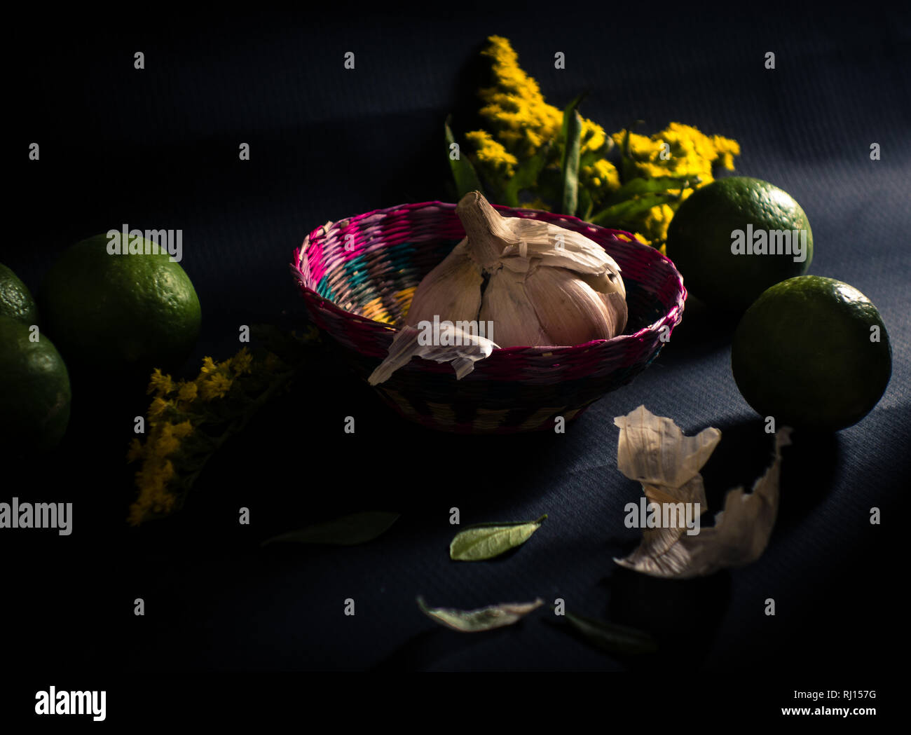 Aglio essiccato lampadina nel cestello con tigli e fiori di colore giallo su sfondo nero - Fotografia scuro Foto Stock