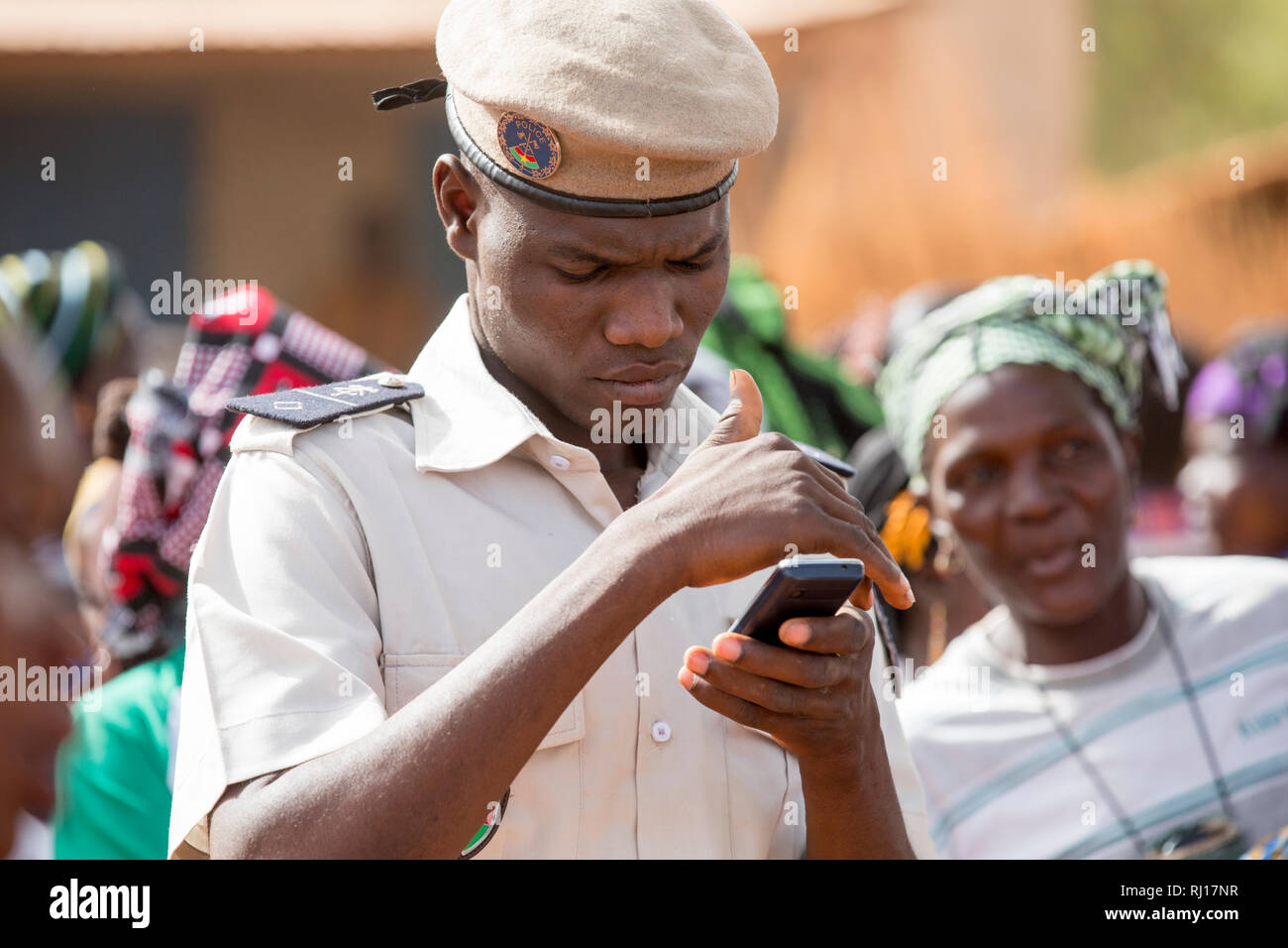 Città Kisi, Burkina Faso; un poliziotto controlla il telefono sulla giornata internazionale della donna una festività nazionale. Foto Stock