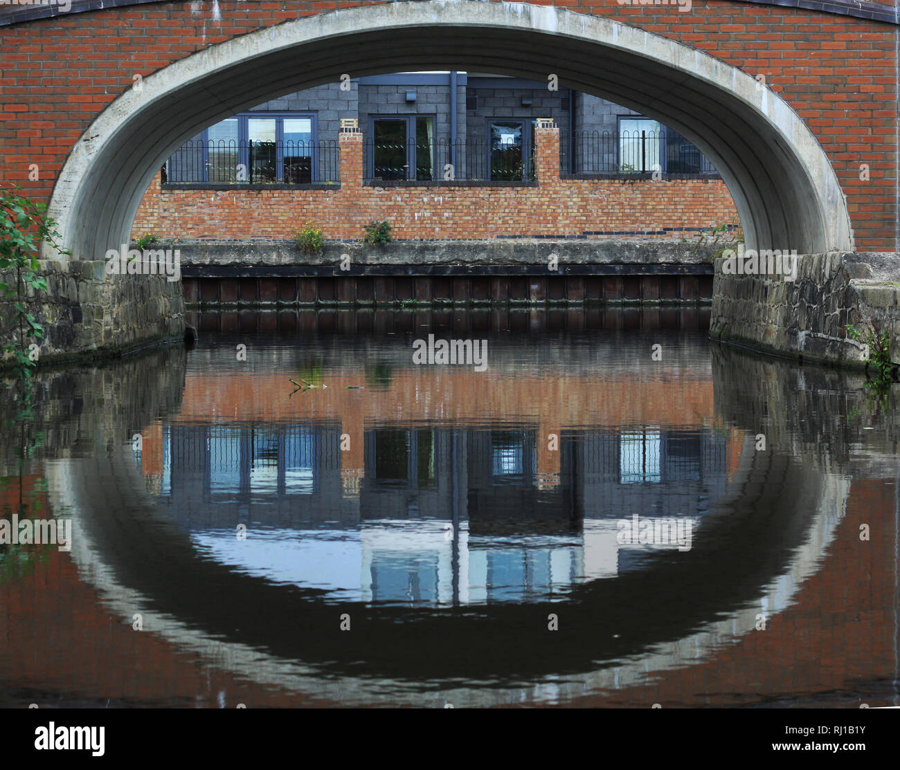 Ponte ad arcate su canal con edifici industriali Foto Stock