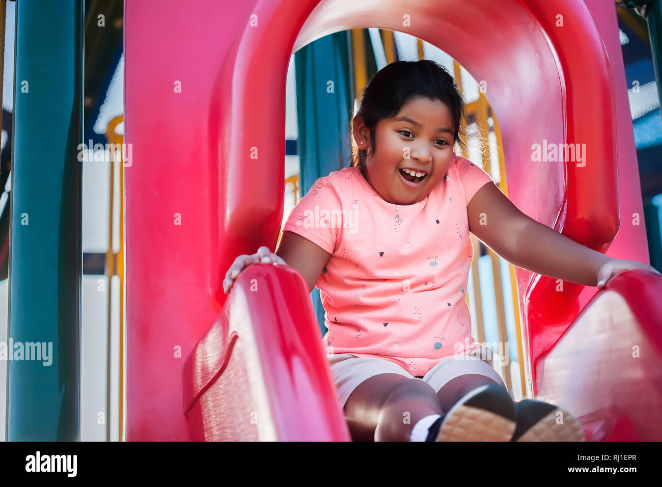 Una ragazza con espressioni di sorpresa, guarda verso il basso dal bordo di un campo giochi diapositiva. Foto Stock