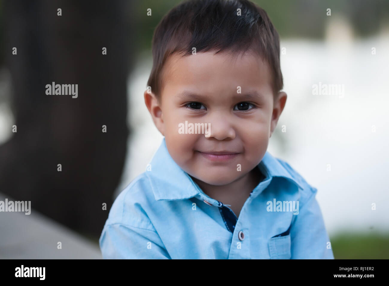 Latino ragazzo indossa maglietta blu e un attenta occhiata, con un sorriso rilassato ma anche guardando incerto. Foto Stock