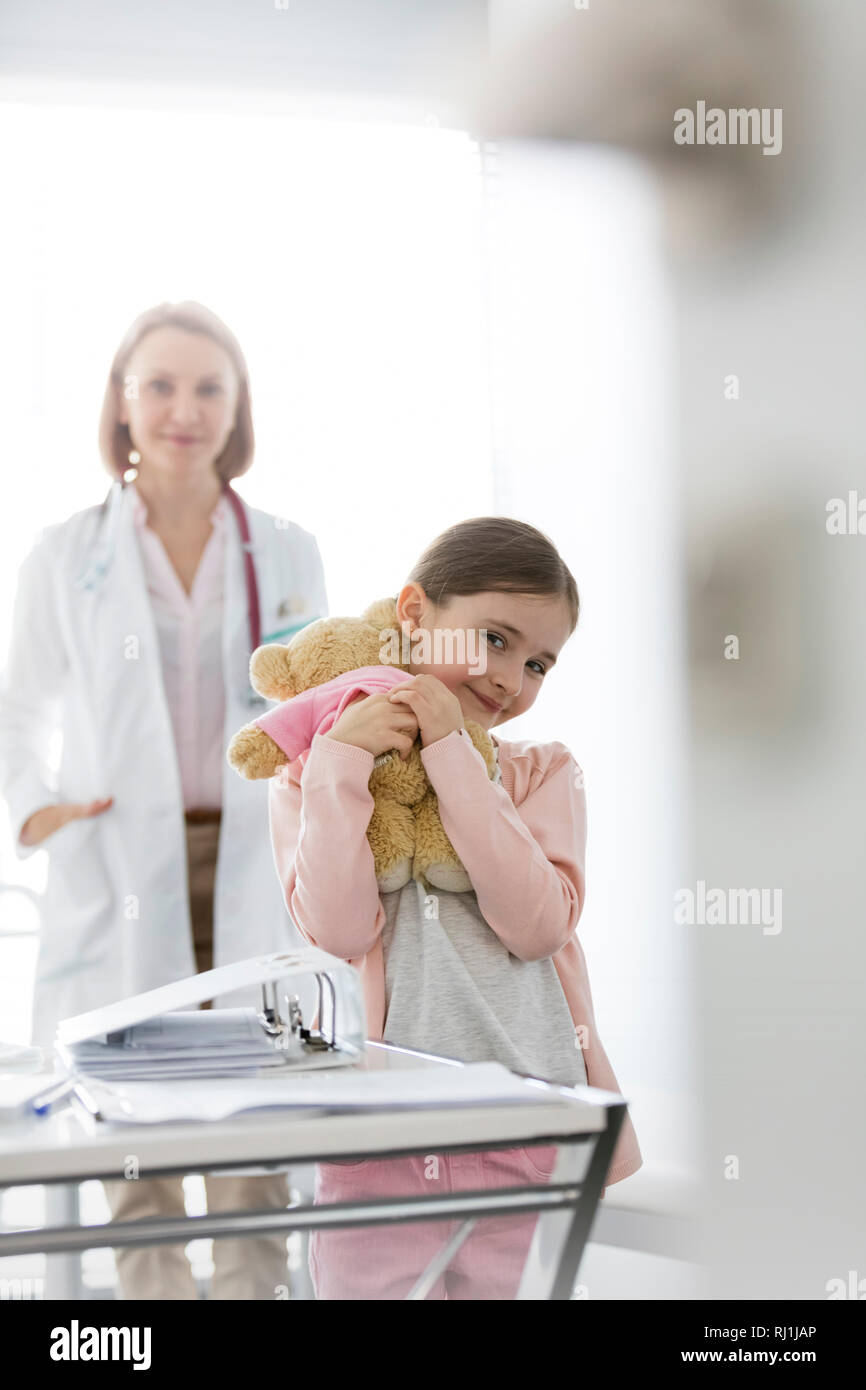 Ritratto di ragazza sorridente con orsacchiotto in piedi contro il medico in ospedale Foto Stock