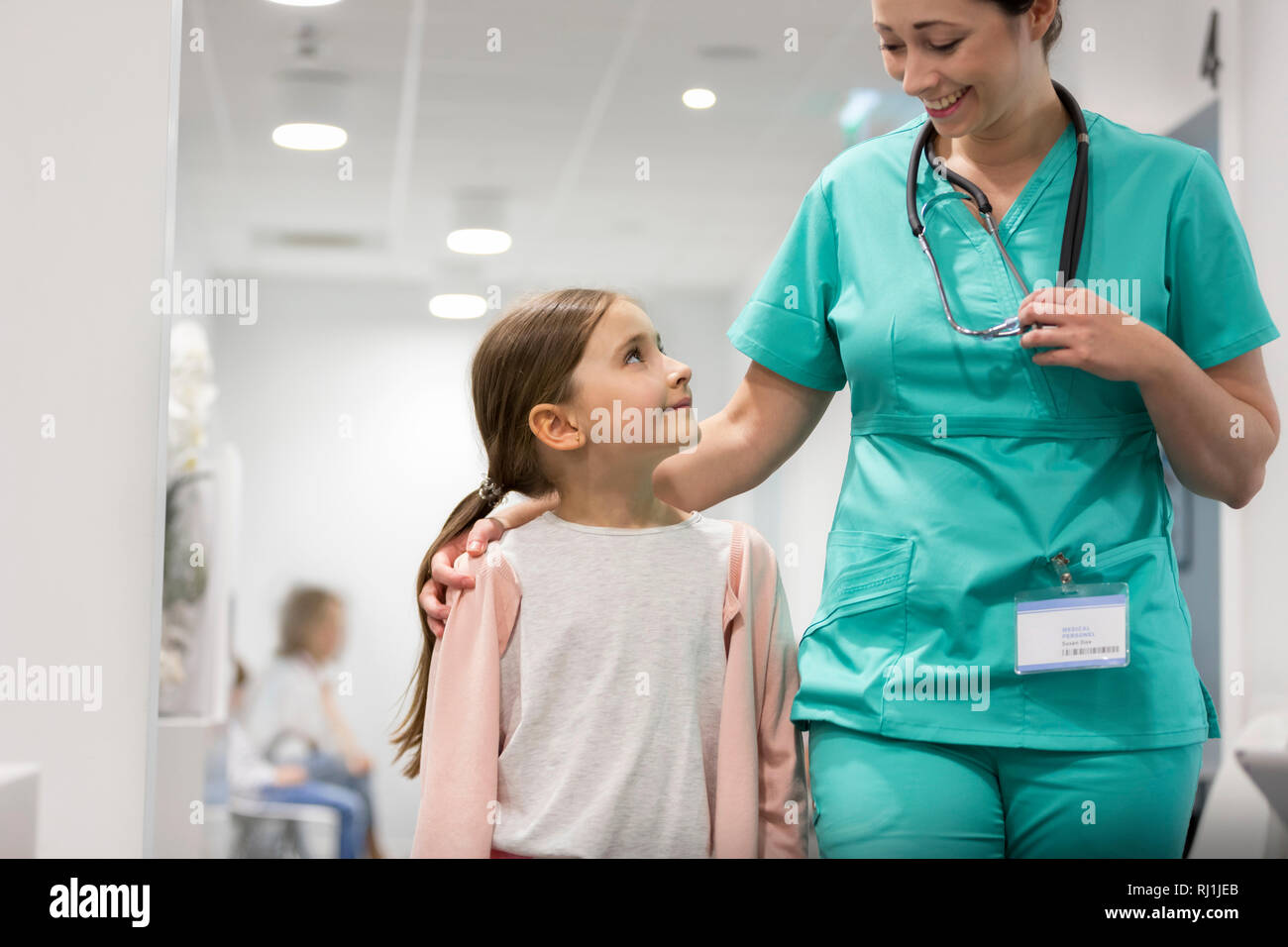 Ragazza sorridente guardando a metà adulto infermiera mentre si cammina nel corridoio di ospedale Foto Stock