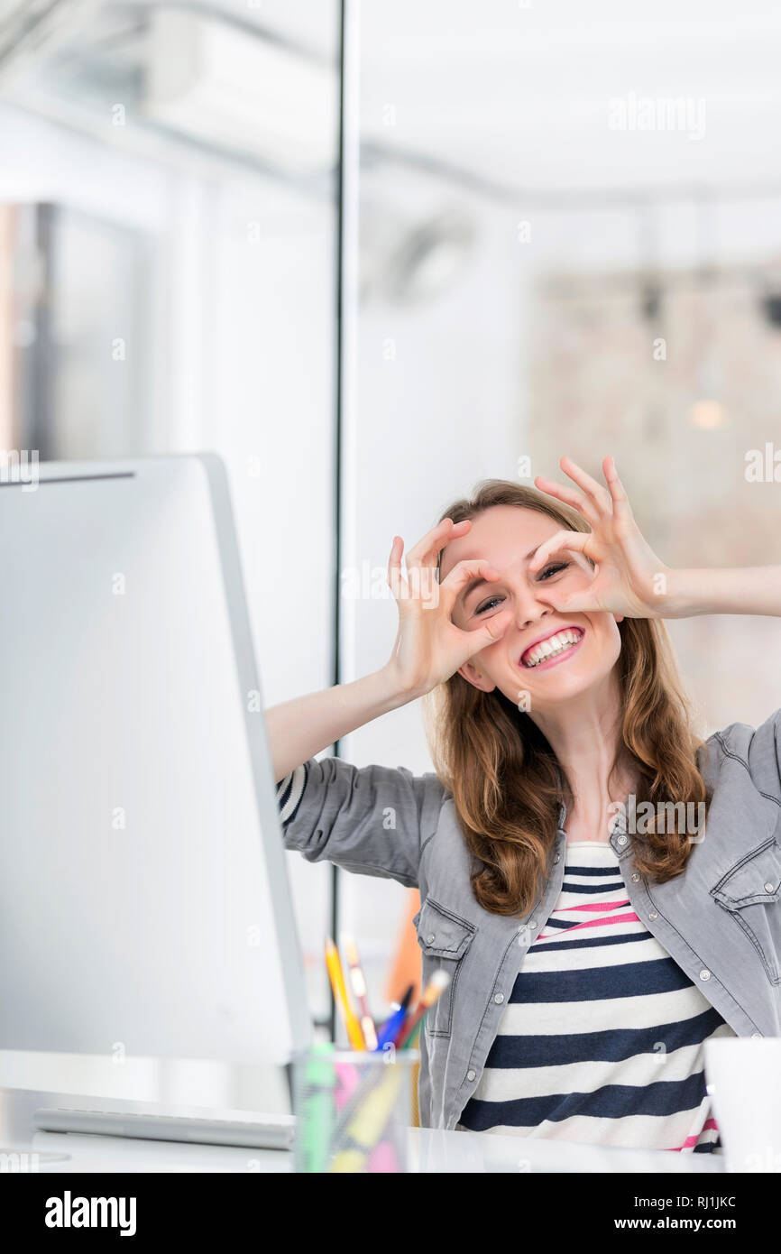 Felice imprenditrice rendendo dito gli occhiali in ufficio Foto Stock