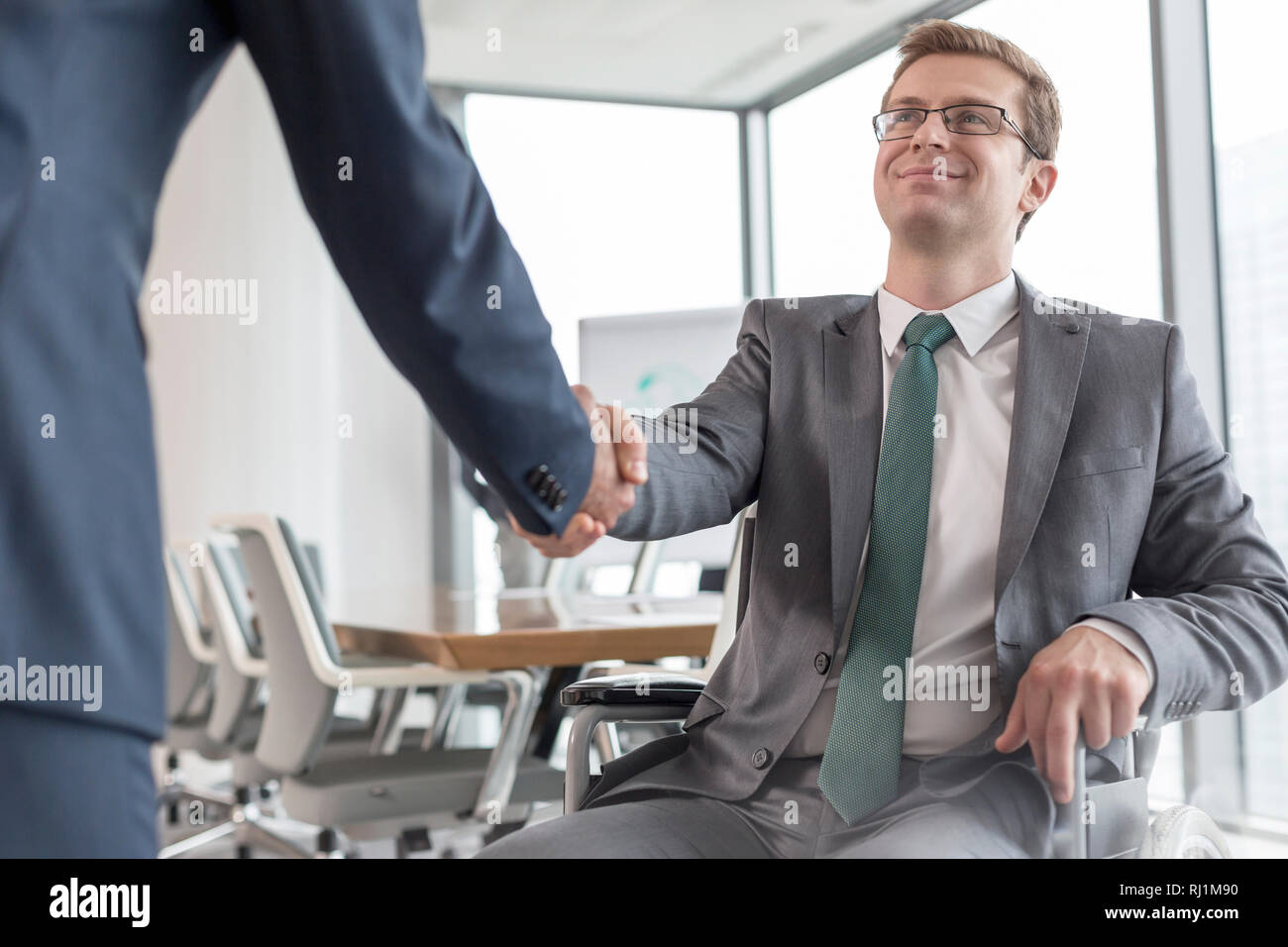 Sorridente imprenditore disabili stringono le mani con il collega in sala riunioni durante la riunione in ufficio Foto Stock
