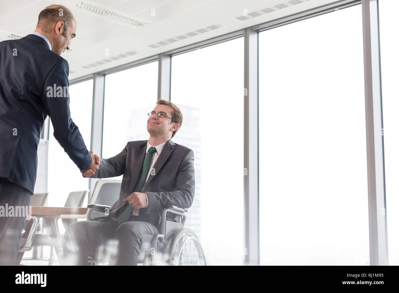 Imprenditore stringono le mani con sorridente disabilitato collega in sala riunioni durante la riunione in ufficio Foto Stock