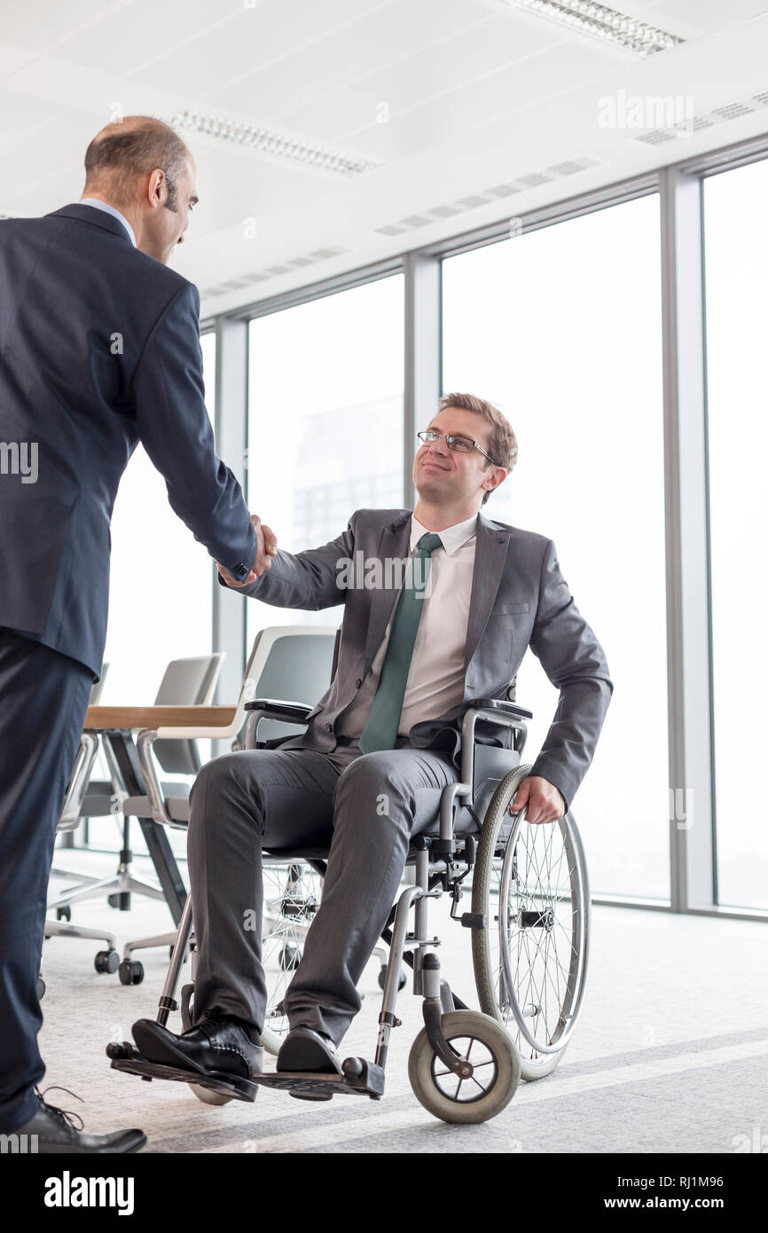 Imprenditore stringono le mani con sorridente collega disabili contro la finestra nella sala riunioni in ufficio Foto Stock