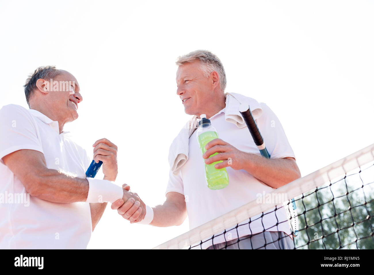 Basso angolo vista di uomini sorridenti si stringono la mano durante il riposo a tennis contro il cielo chiaro sulla giornata di sole Foto Stock