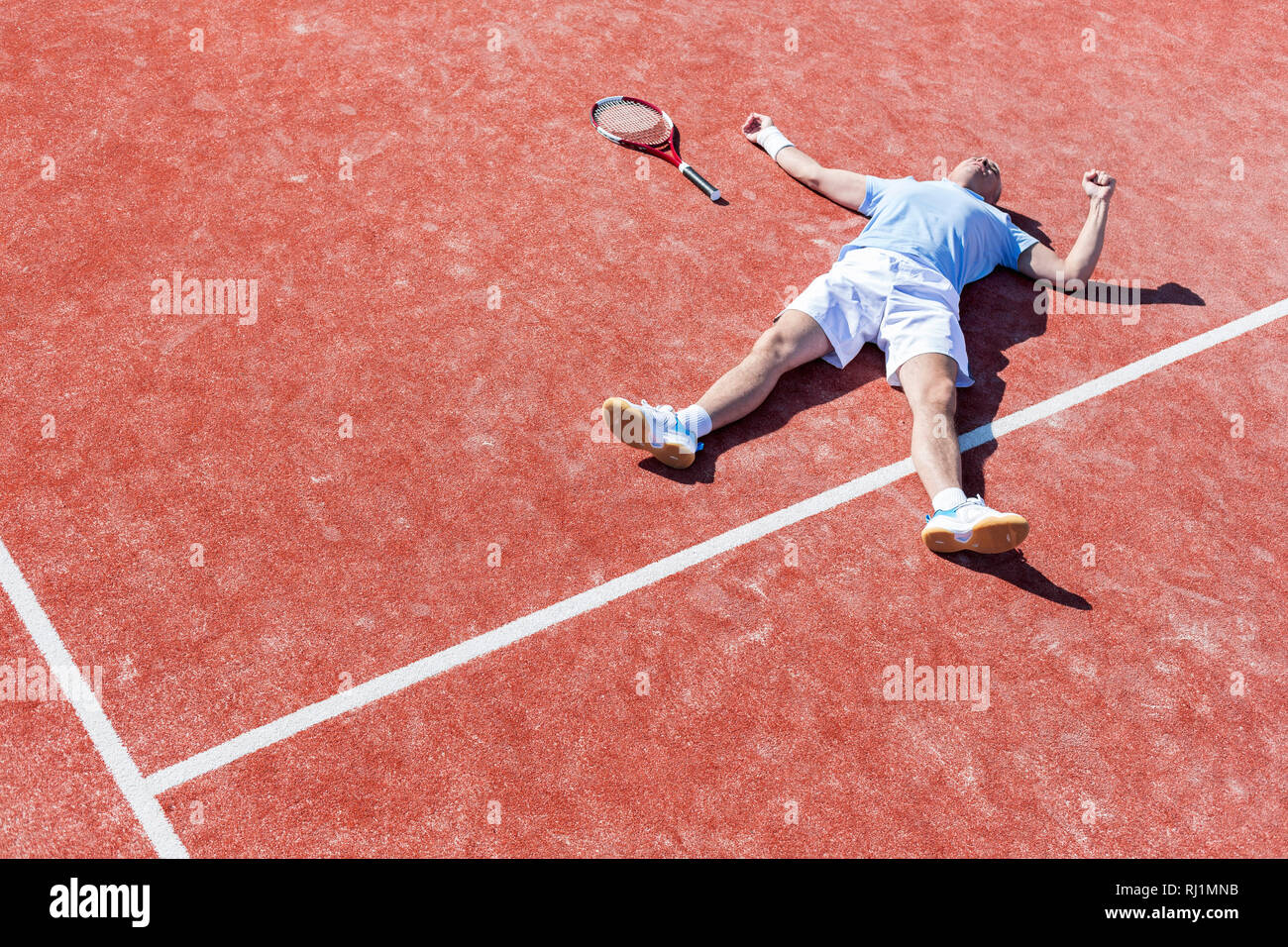 Lunghezza completa di deluso uomo maturo giacenti da racchetta da tennis su corte durante la stagione estiva Foto Stock