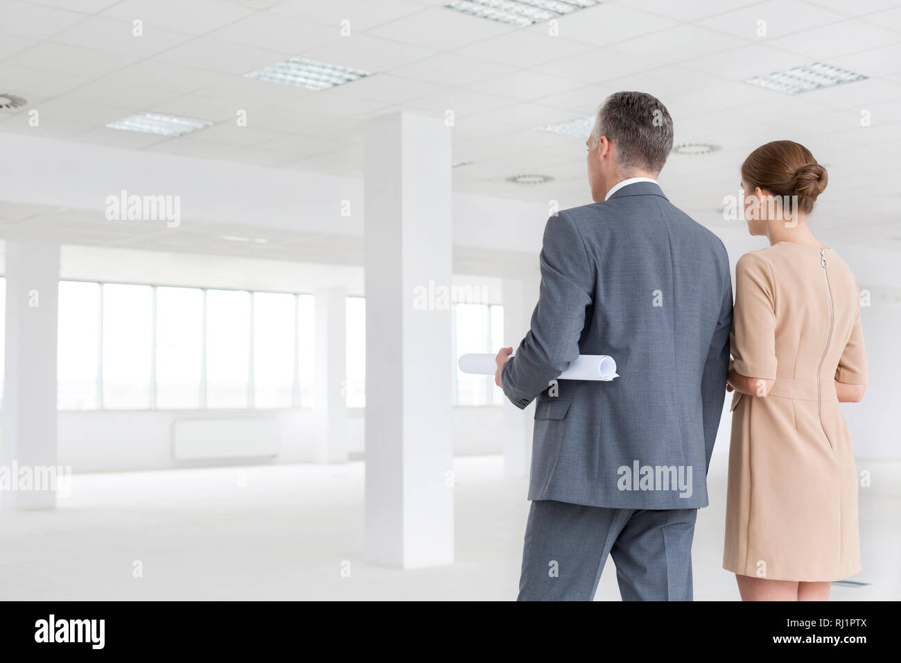 Vista posteriore di imprenditore e imprenditrice in piedi nel nuovo ufficio vuoto Foto Stock