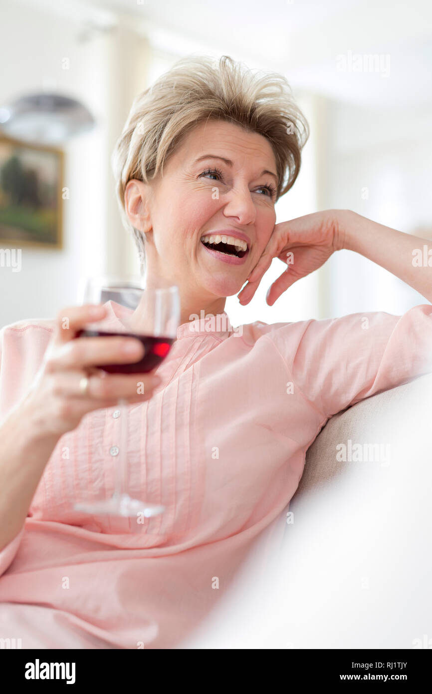 Allegra donna matura azienda wineglass mentre guarda lontano da casa Foto Stock