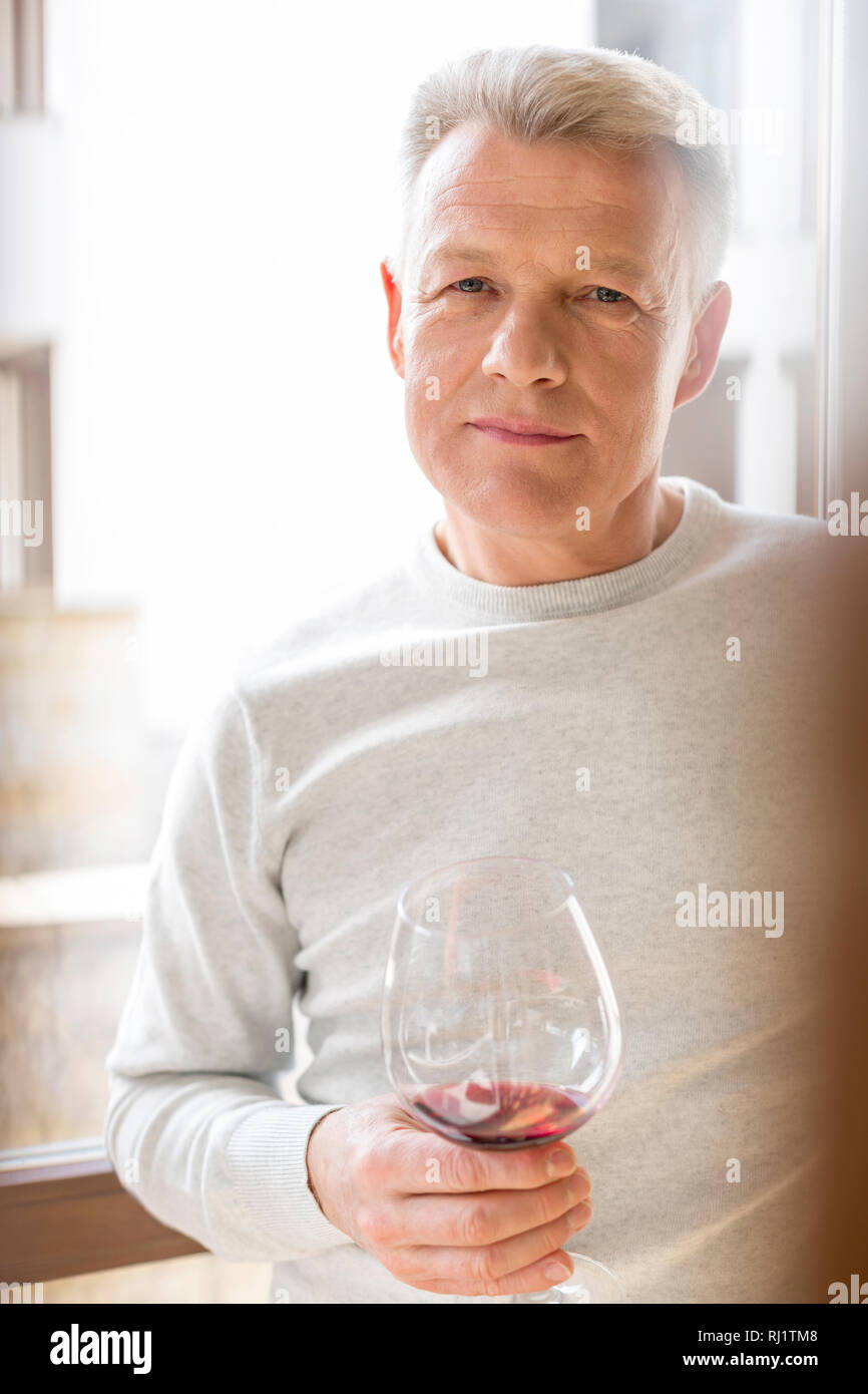 Ritratto di uomo maturo holding wineglass in piedi a casa Foto Stock