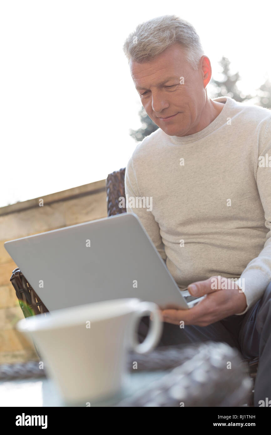 Uomo maturo utilizzando computer portatile mentre è seduto al patio Foto Stock