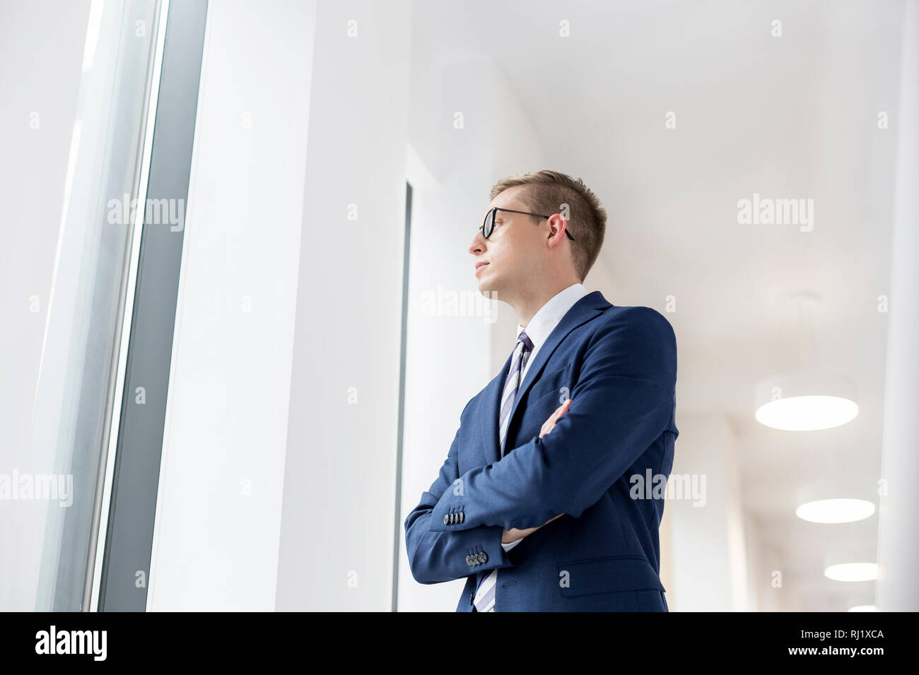 Giovane imprenditore pensieroso in piedi con le braccia incrociate nel corridoio di office Foto Stock