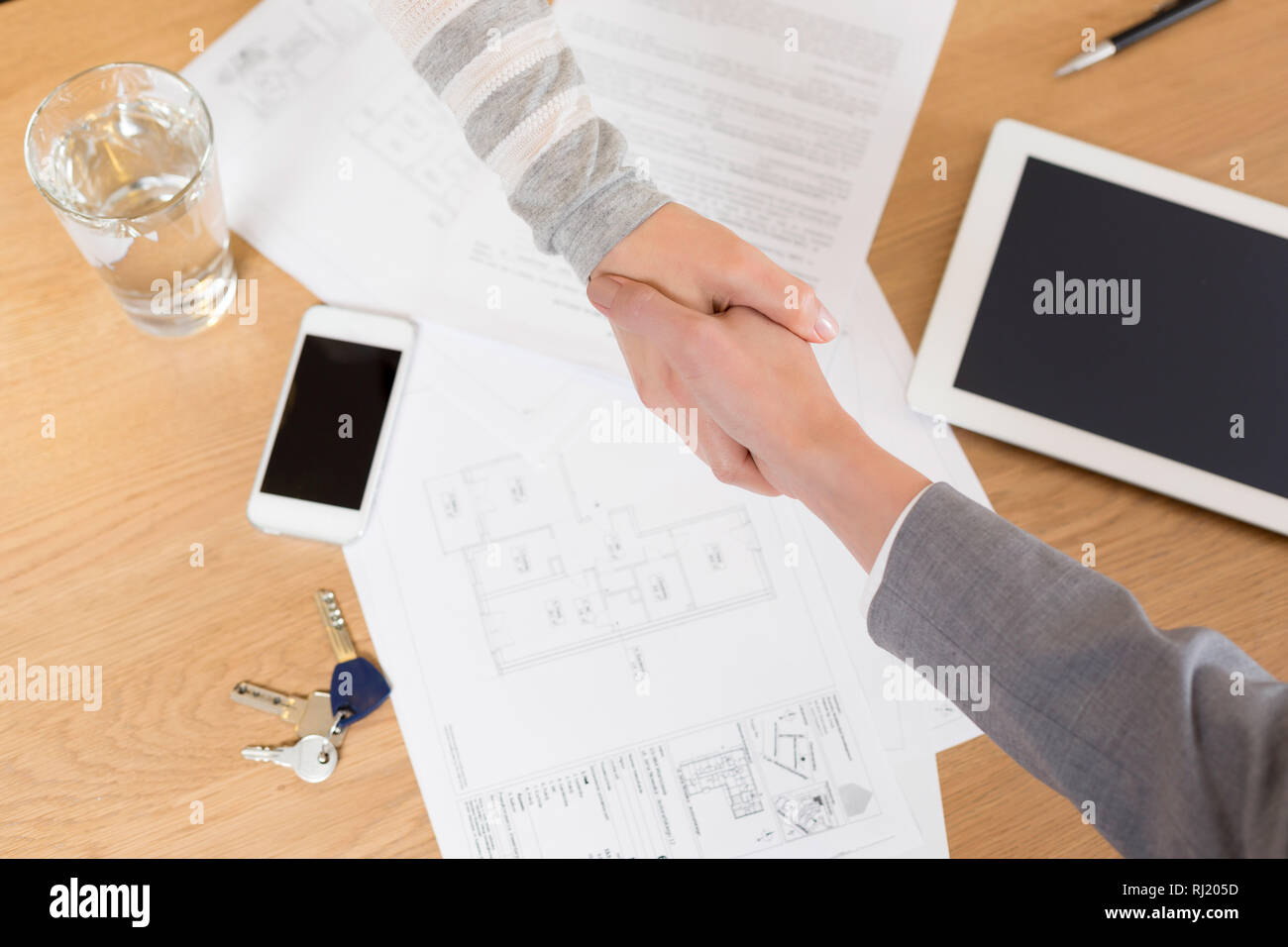 Angolo di Alta Vista della commessa e il client stringono le mani su documenti sulla tavola in appartamento Foto Stock