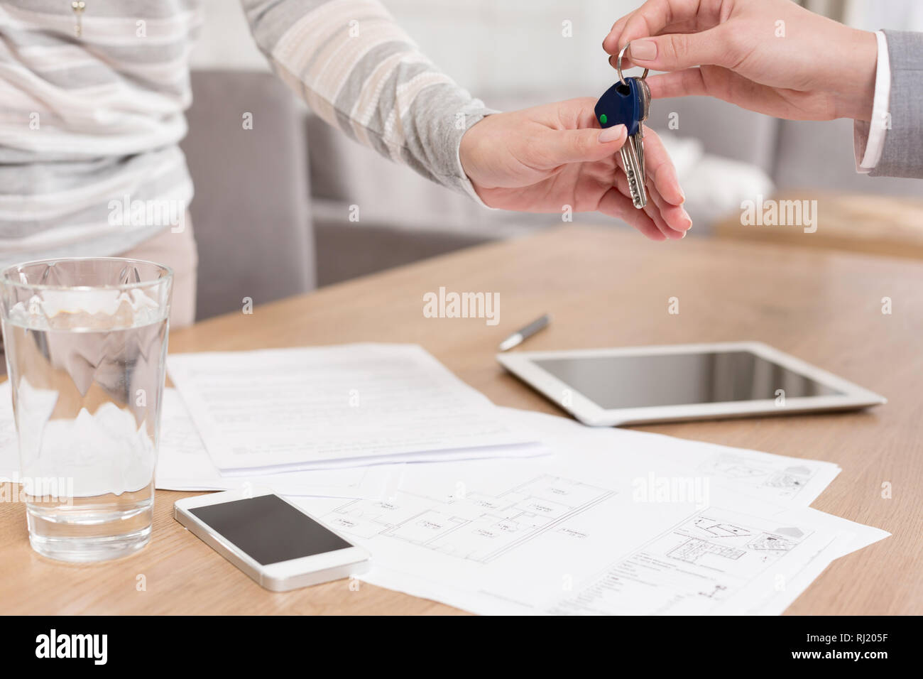 Mano di commessa di dare le chiavi di casa a femmina client in documenti sulla tavola in appartamento Foto Stock