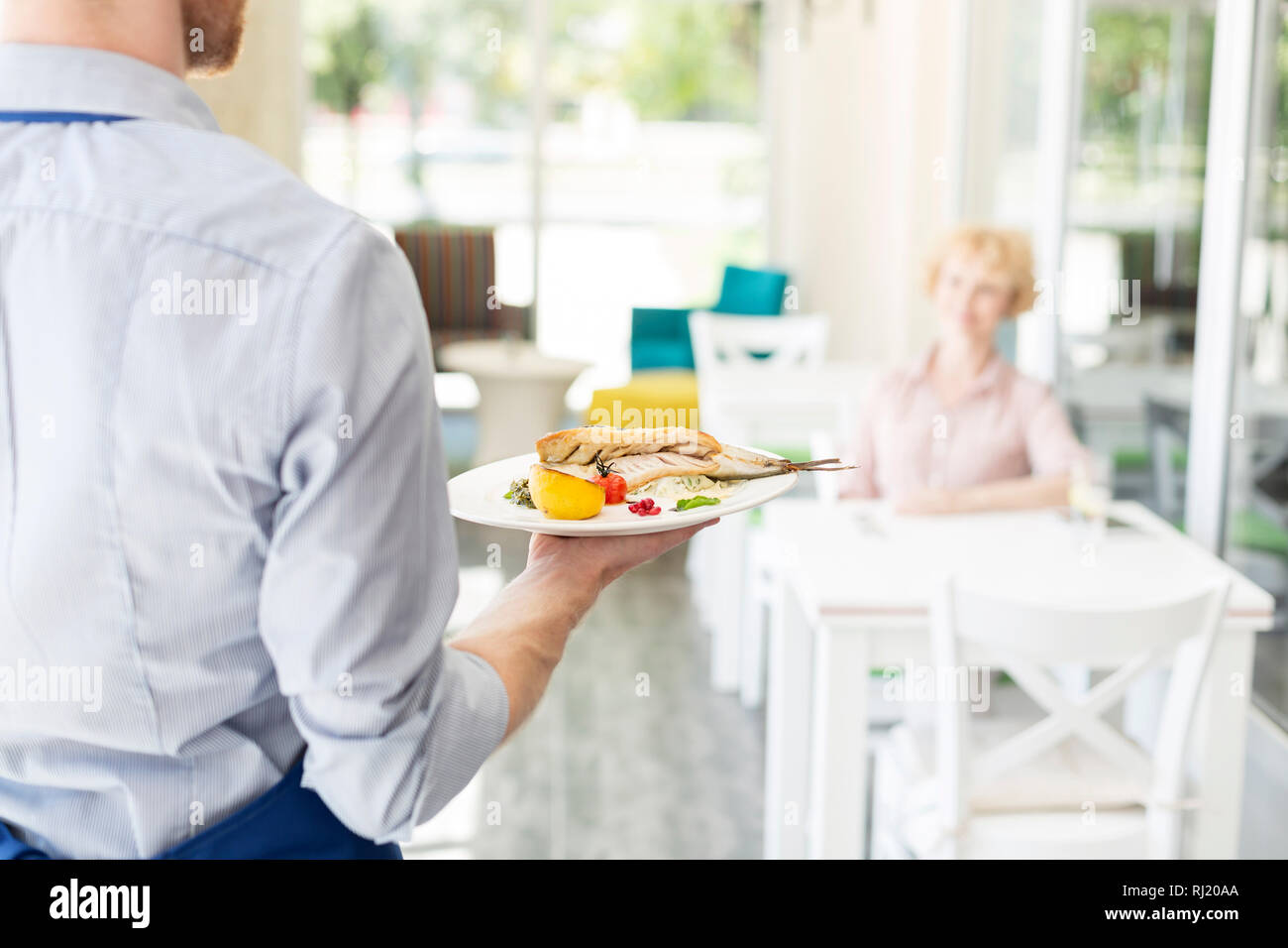 Sezione mediana del cameriere che serve il pranzo a maturare il cliente seduto al tavolo nel ristorante Foto Stock