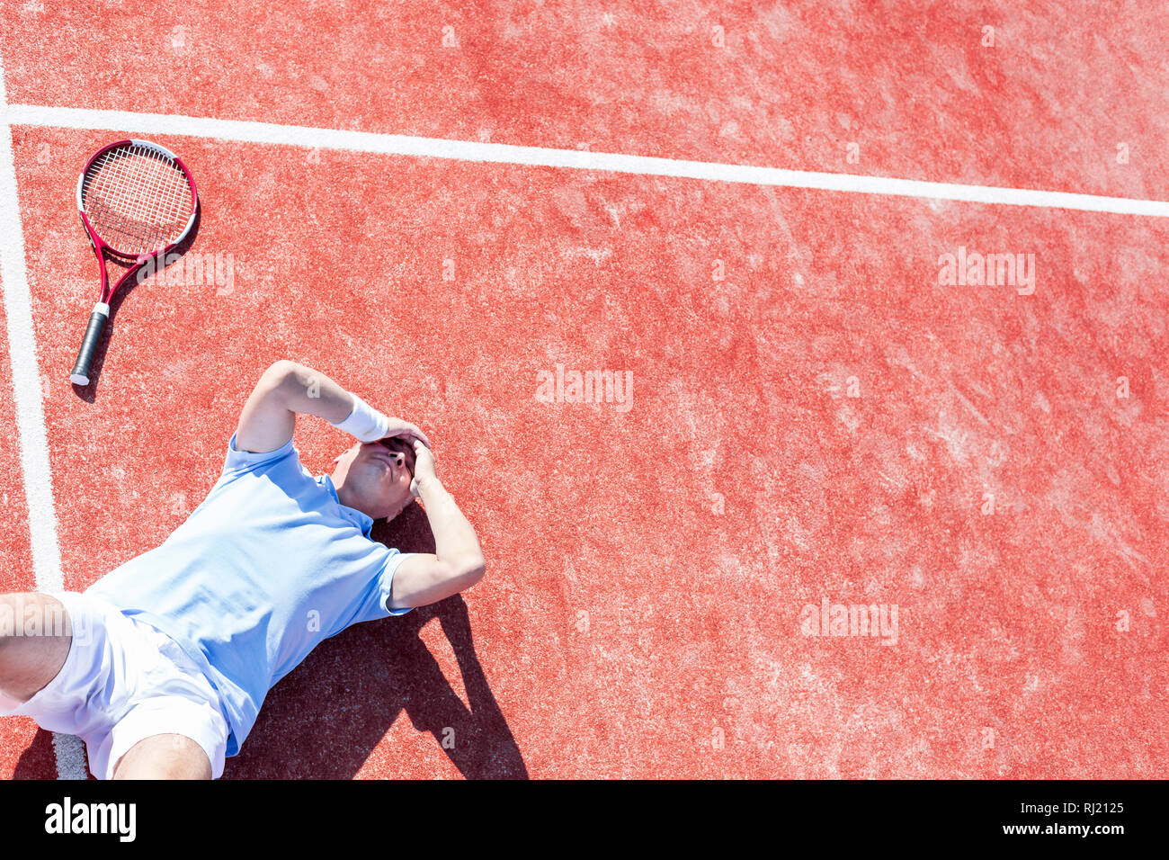 Elevato angolo di visione dei delusi uomo maturo con testa in mani mentre giaceva da racchetta da tennis su corte durante la stagione estiva Foto Stock