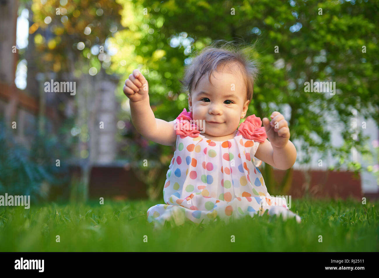 Happy funny Baby girl sedersi su erba verde sullo sfondo Foto Stock