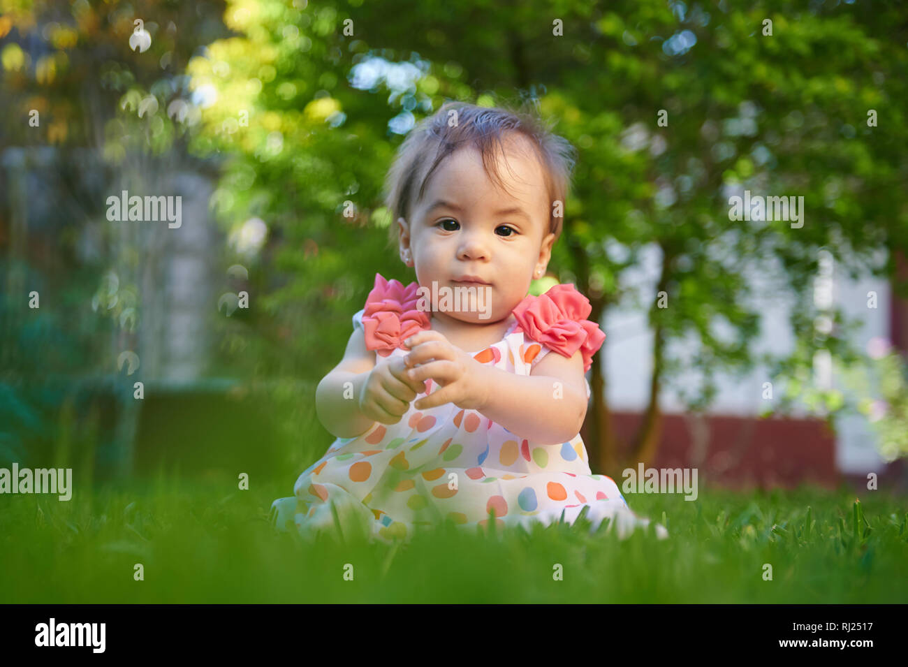 Ritratto di bambina seduta su erba verde sullo sfondo Foto Stock