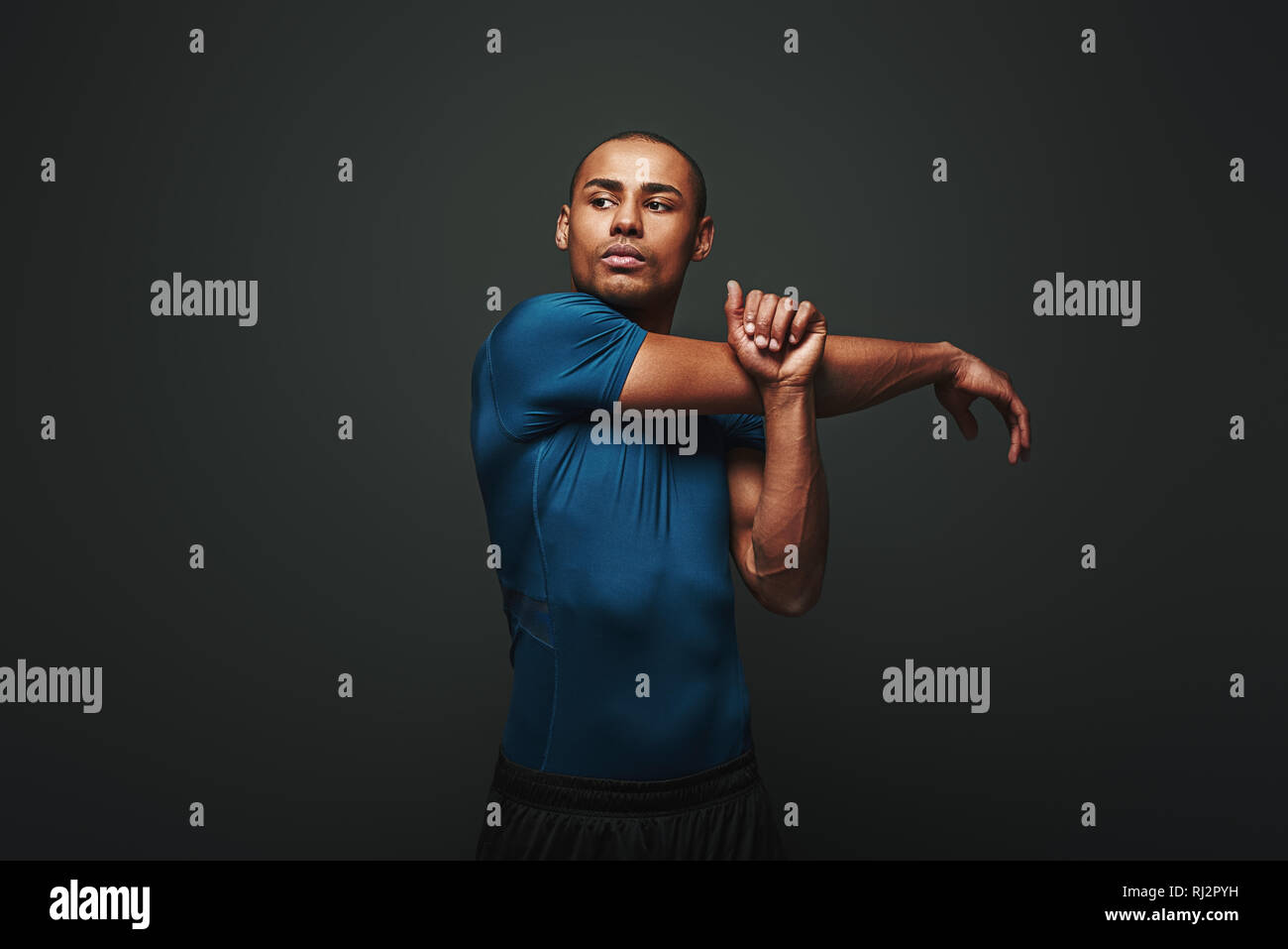 Ritratto di giovane forte uomo muscolare stretching le sue braccia. Africa Fitness modello maschile in piedi su sfondo scuro Foto Stock