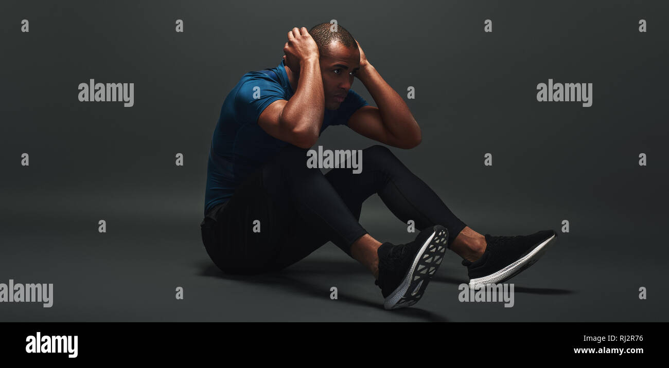 Dark scuoiati uomo in abbigliamento sportivo è concentrata durante il funzionamento del sistema ABS, giacente su sfondo scuro. A piena lunghezza Foto Stock