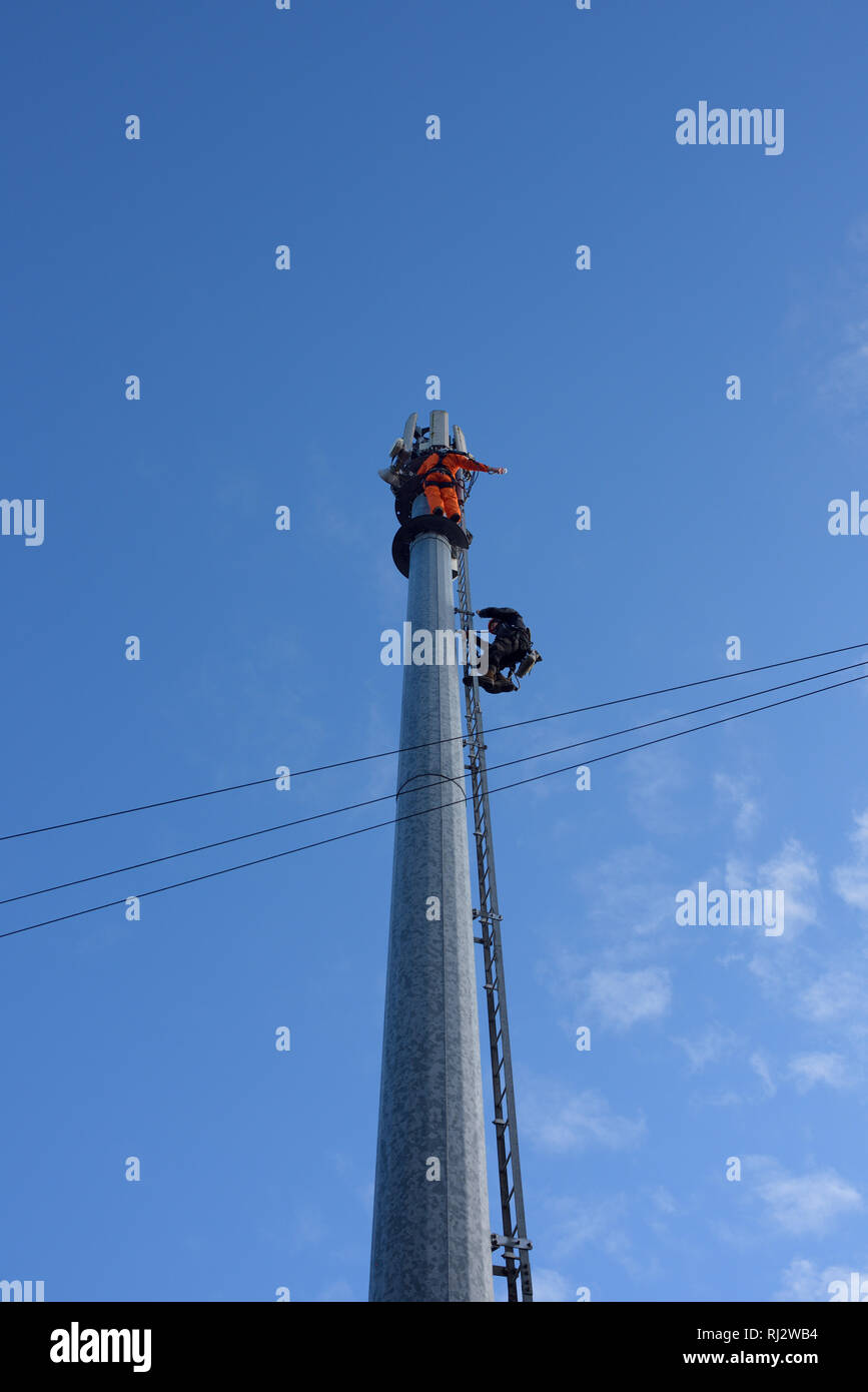 Due ingegneri di telecomunicazioni che lavorano in quota su un palo per telefoni cellulari da 5 g con cielo blu a Bury lancashire regno unito Foto Stock