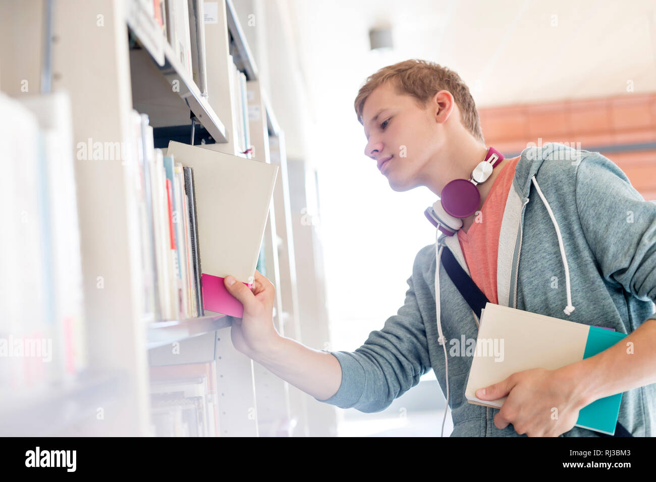 Giovane uomo ricerca per prenotare presso la Biblioteca universitaria Foto Stock