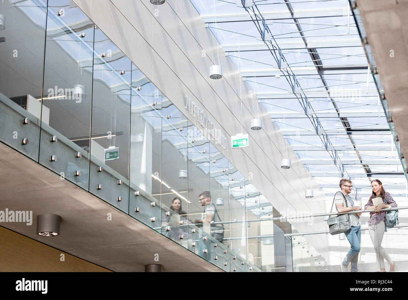 Basso angolo di visione degli studenti di parlare mentre si sta in piedi sul pavimento di vetro al campus universitario Foto Stock
