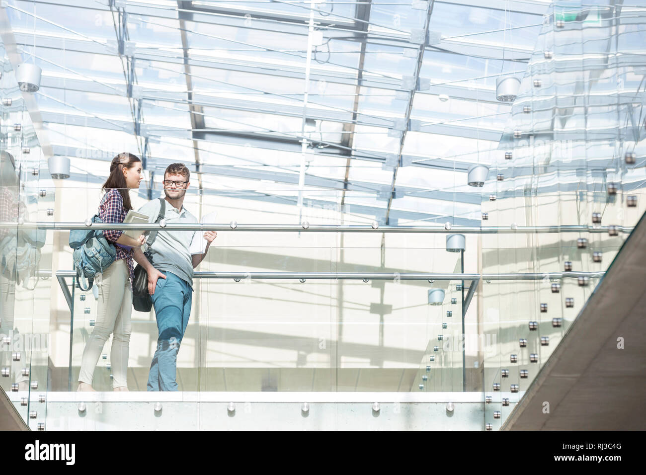 Basso angolo di visione degli studenti di parlare mentre si cammina sul pavimento di vetro al campus universitario Foto Stock