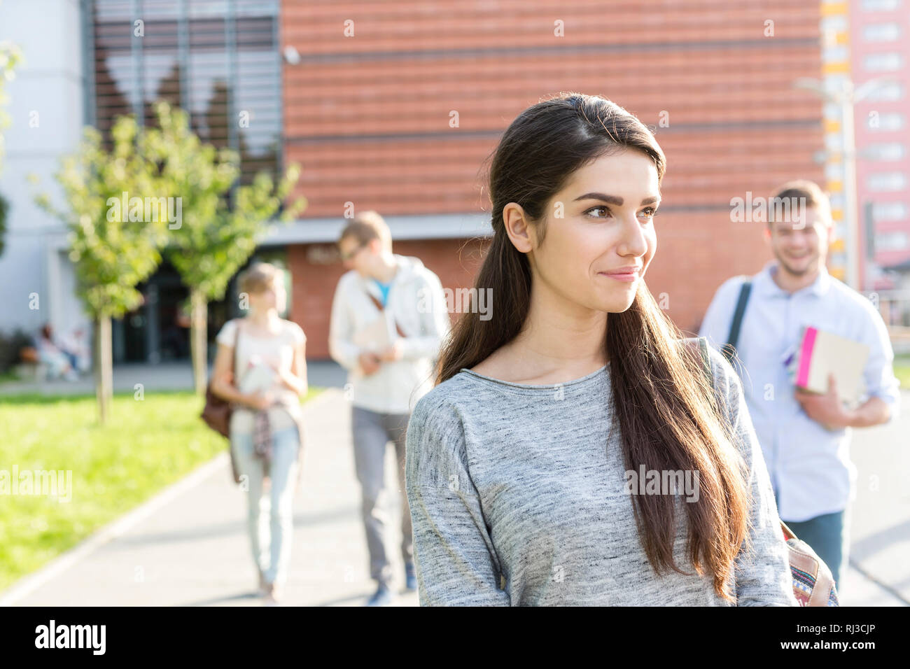 Sorridente ragazza adolescente che guarda lontano mentre si cammina con gli amici al campus universitario Foto Stock