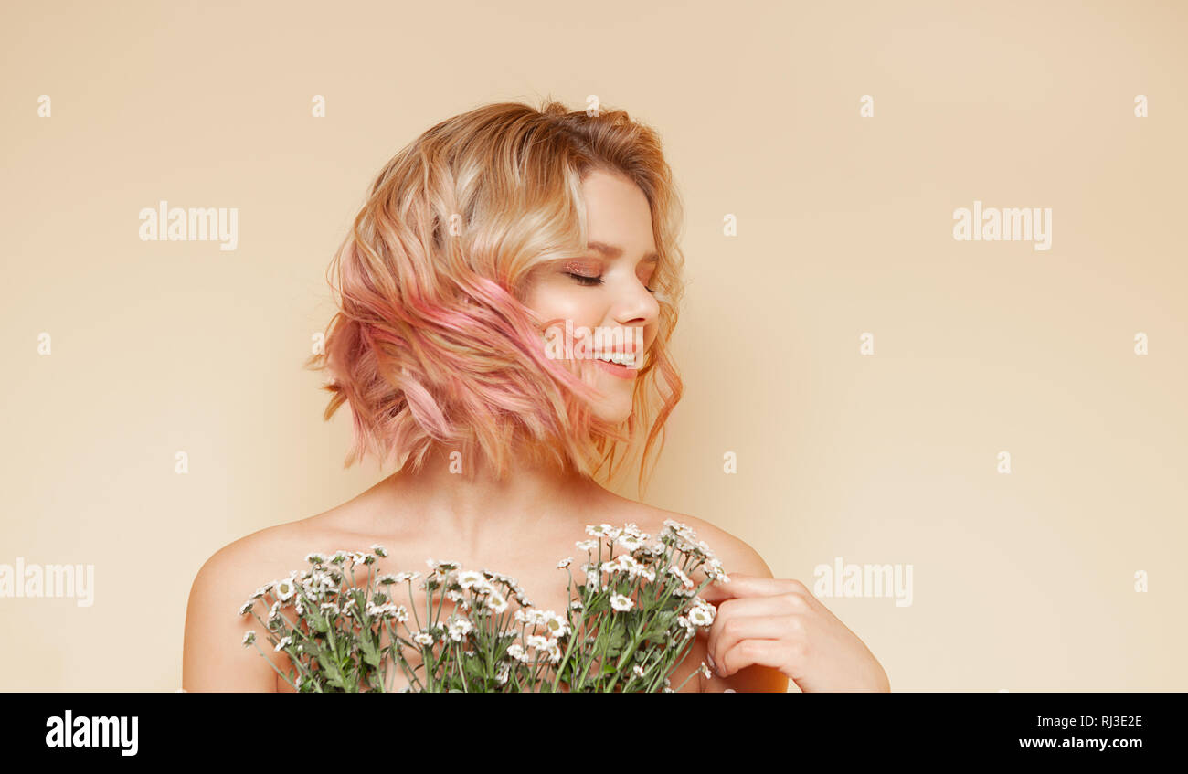 Giovane donna tanga con colorazione rosa battenti capelli ricci e fiori selvatici sorridente Foto Stock