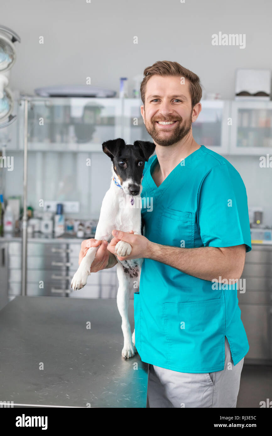 Ritratto di sorridente medico veterinario in piedi con cane in clinica e sorridente alla fotocamera Foto Stock