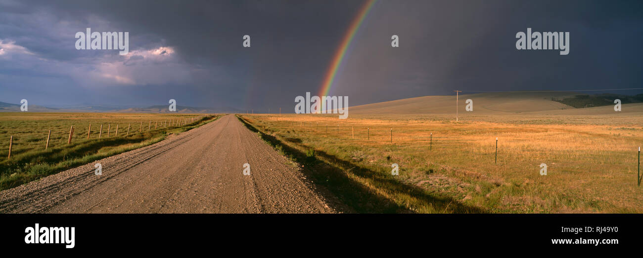 Stati Uniti d'America, Montana, Beaverhead County, arcobaleno e nuvole scure su remote strada di ghiaia e rangeland. Foto Stock