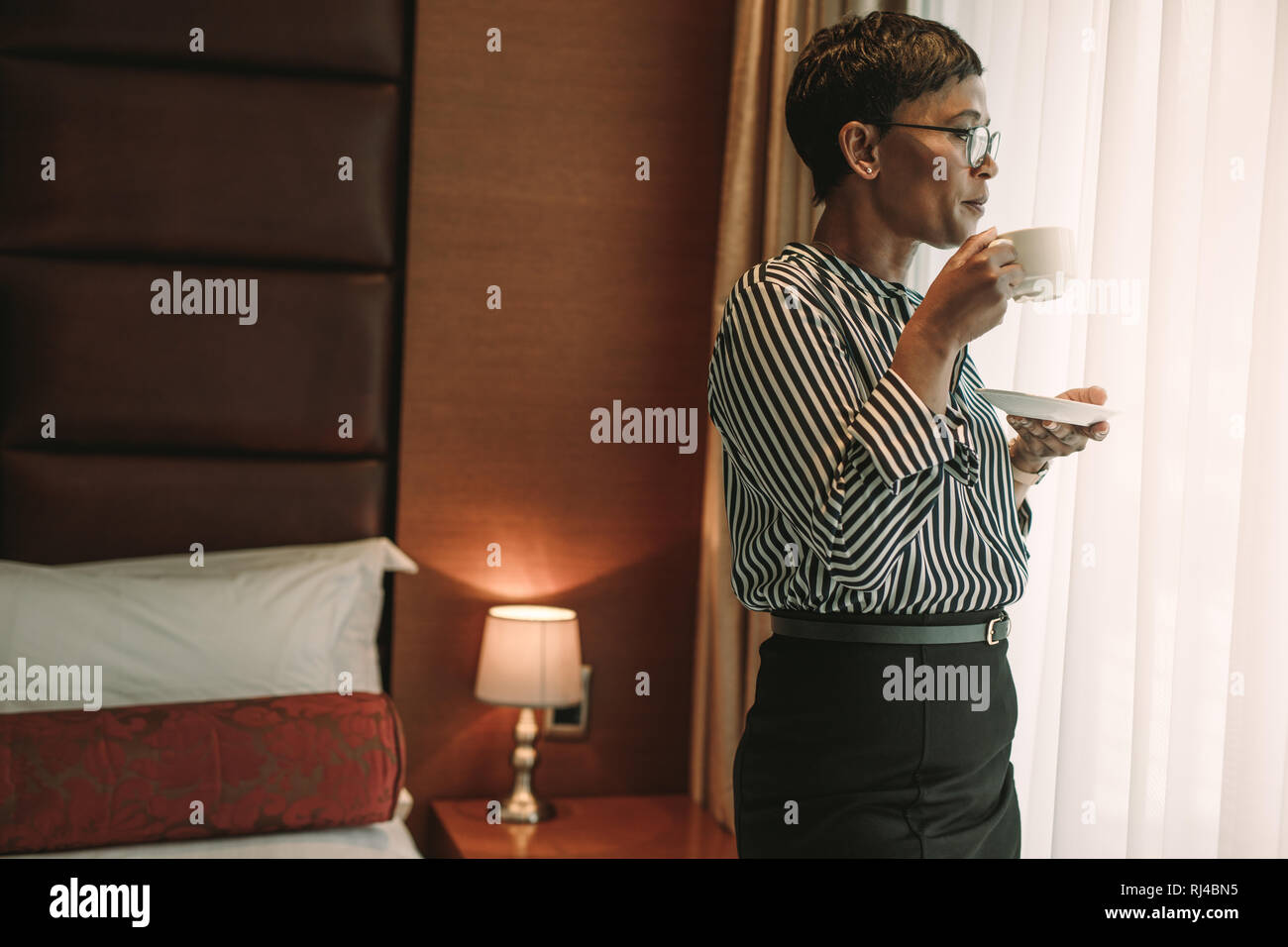 Coppia donna africana in abiti formali in piedi nella camera di albergo e avente una tazza di caffè. Imprenditrice in piedi nella camera di albergo di bere il caffè. Foto Stock