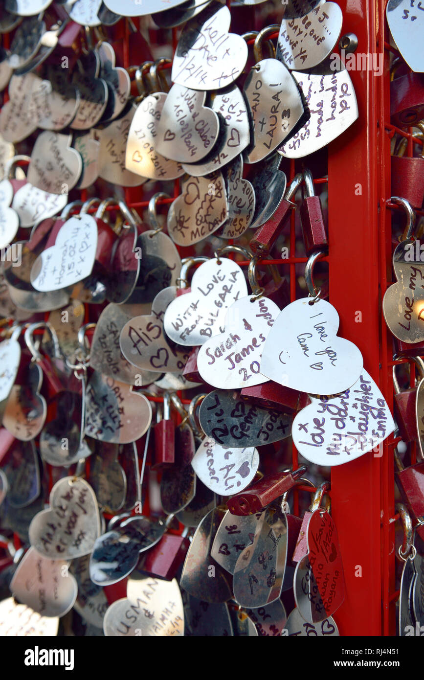 Liebesschlösser und beschriebene Herzen aus Metall hängen un einem roten Gestell Foto Stock