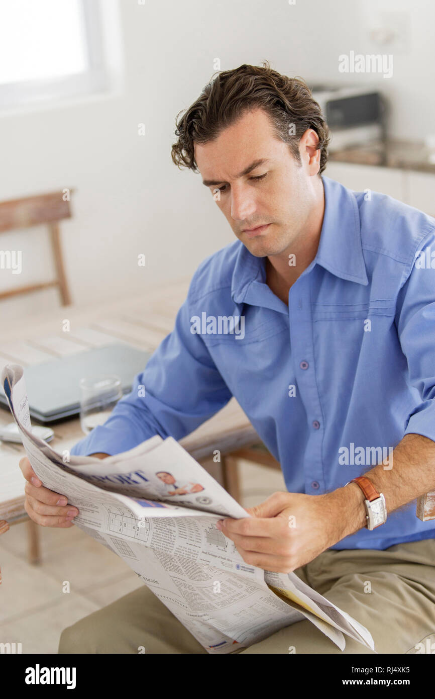 Mann sitzt am Tisch und liest in Zeitung Foto Stock