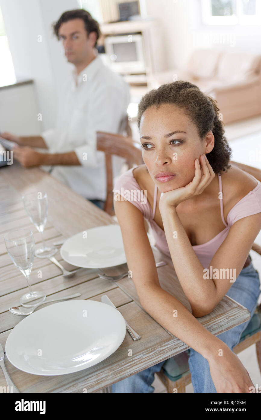 Nachdenkliche junge Frau am Tisch, Mann unscharf im Hintergrund Foto Stock