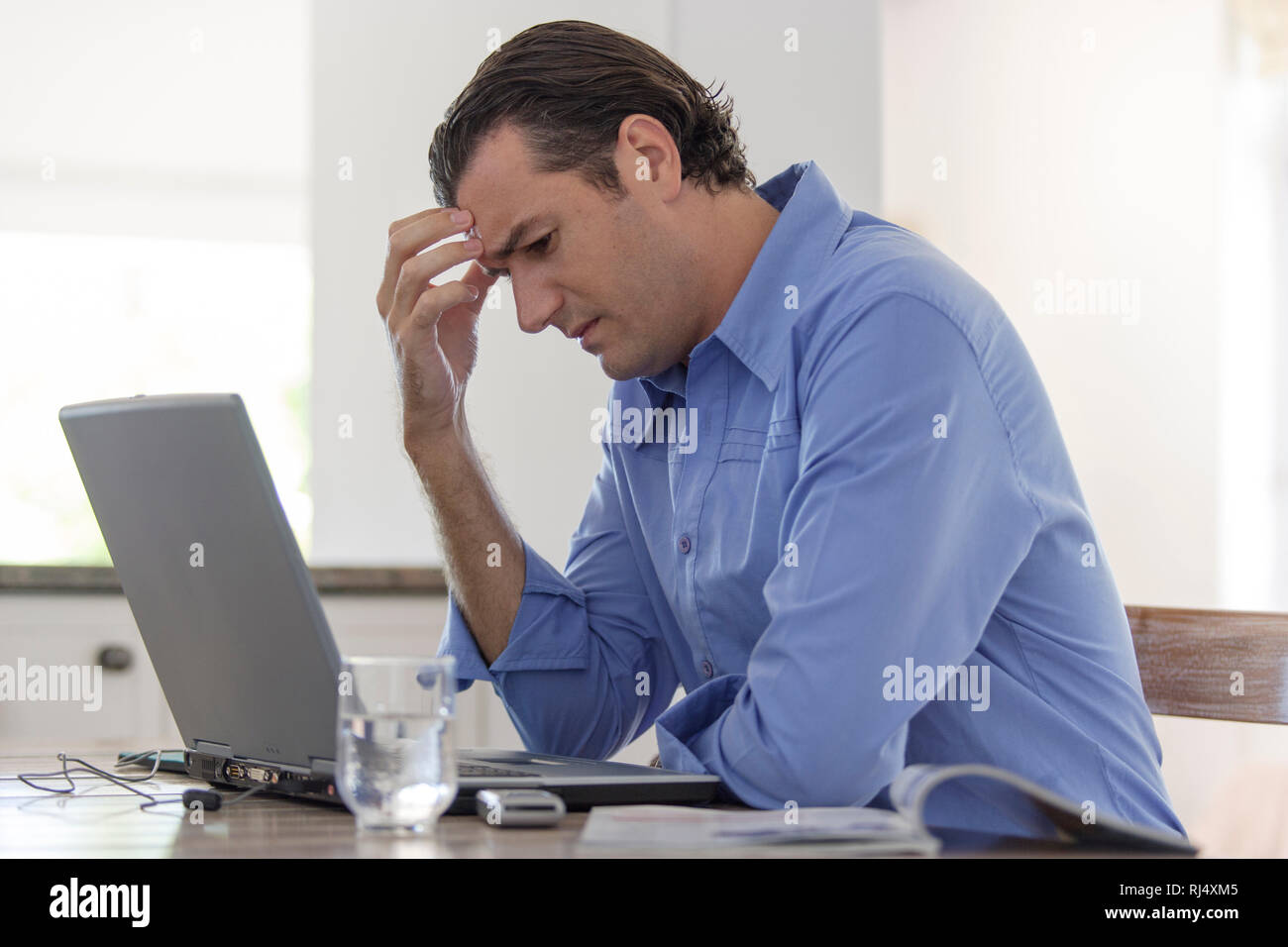 Nachdenklicher Mann sitzt am Tisch mit Laptop Foto Stock