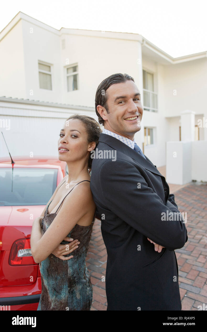 Paar steht Rücken un Rücken vor Auto und Haus Foto Stock