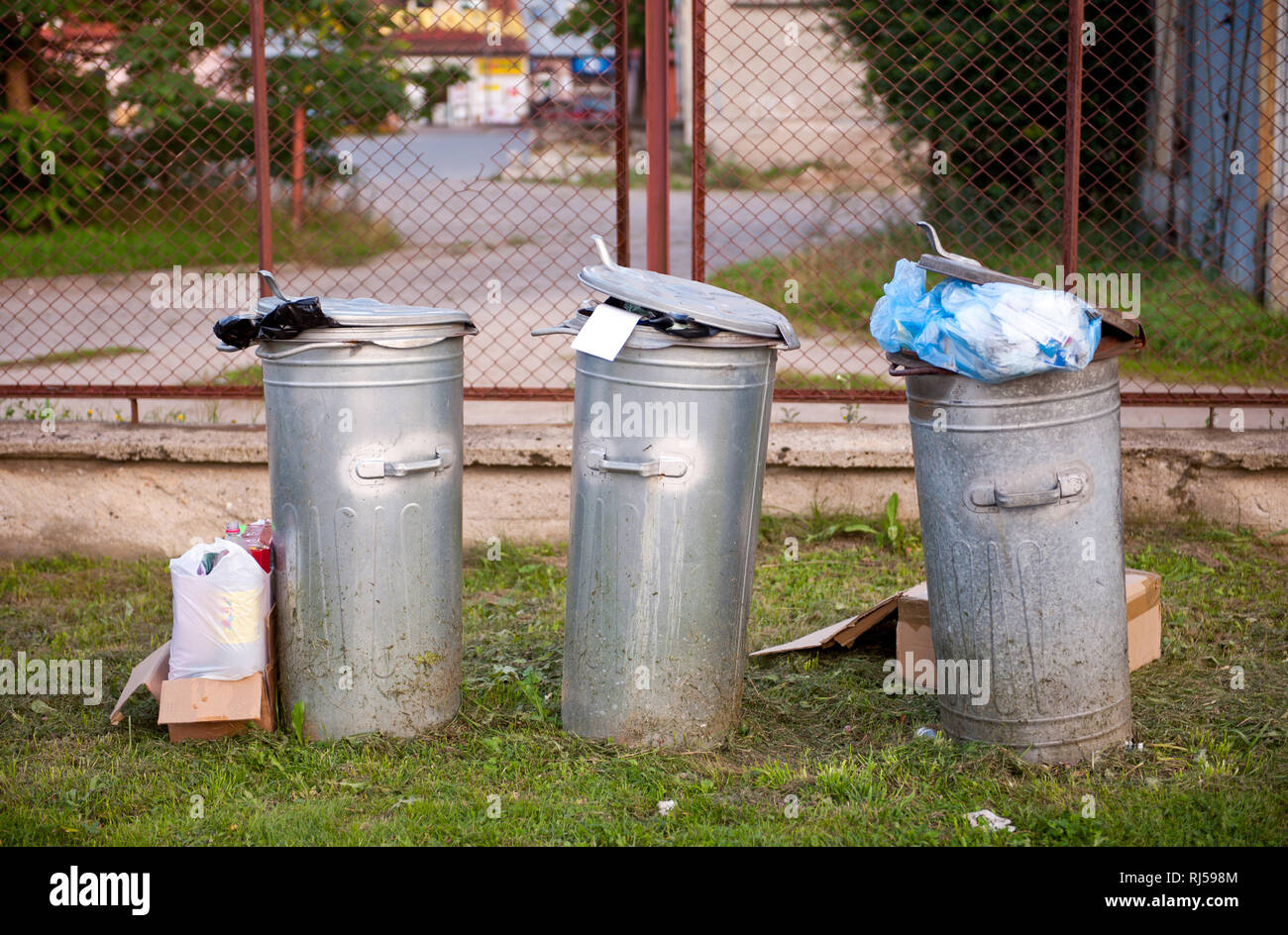 Garbage in tre ceste, tin completo contenitori awry permanente su erba e recinto rosso dietro, oggetti in Polonia, Europa, nessuno, Foto Stock