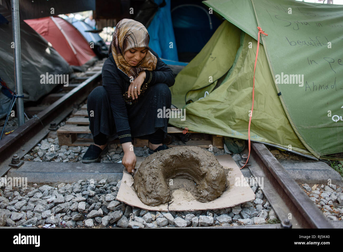 Eine Frau baut sich eine Feuerstelle Lehm aus. Flüchtlingscamp von Idomeni in Griechenland an der Grenze nach Mazedonien, aprile 2016. Foto Stock