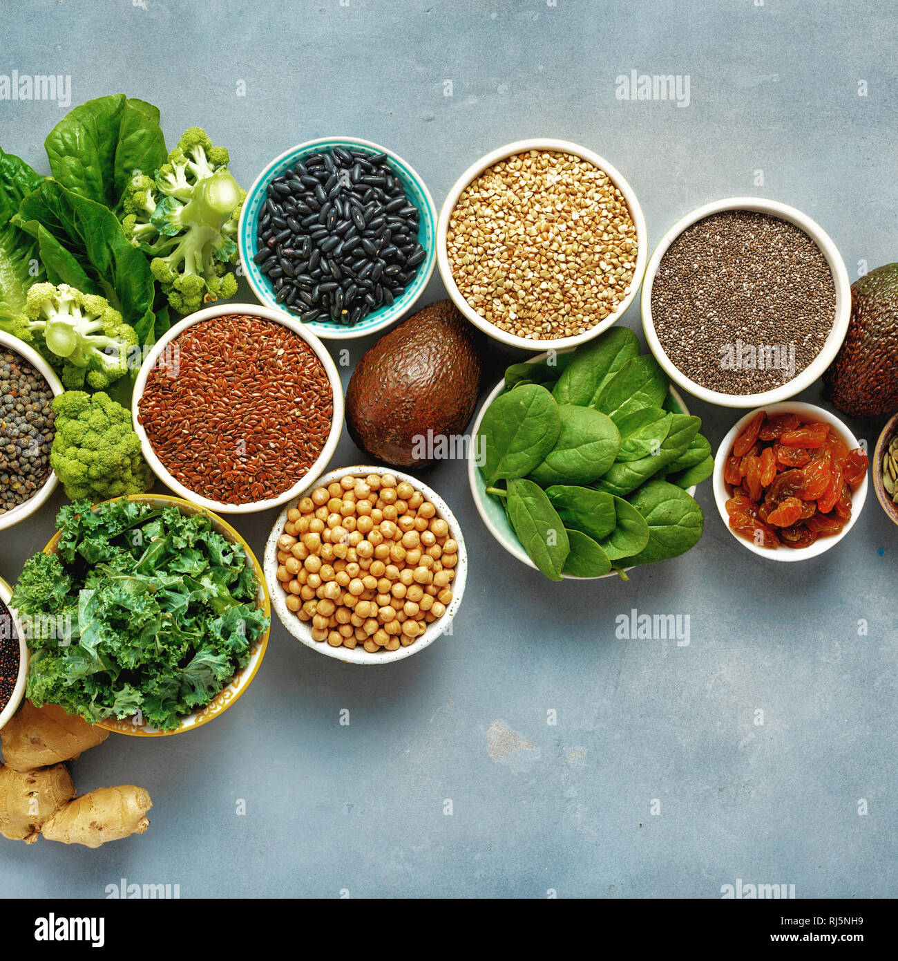 Vegetariano cibo sano concetto. Impostare materie semi, cereali, fagioli, superfoods e verdura verde sulla pietra blu sullo sfondo vista superiore laici piatta Foto Stock