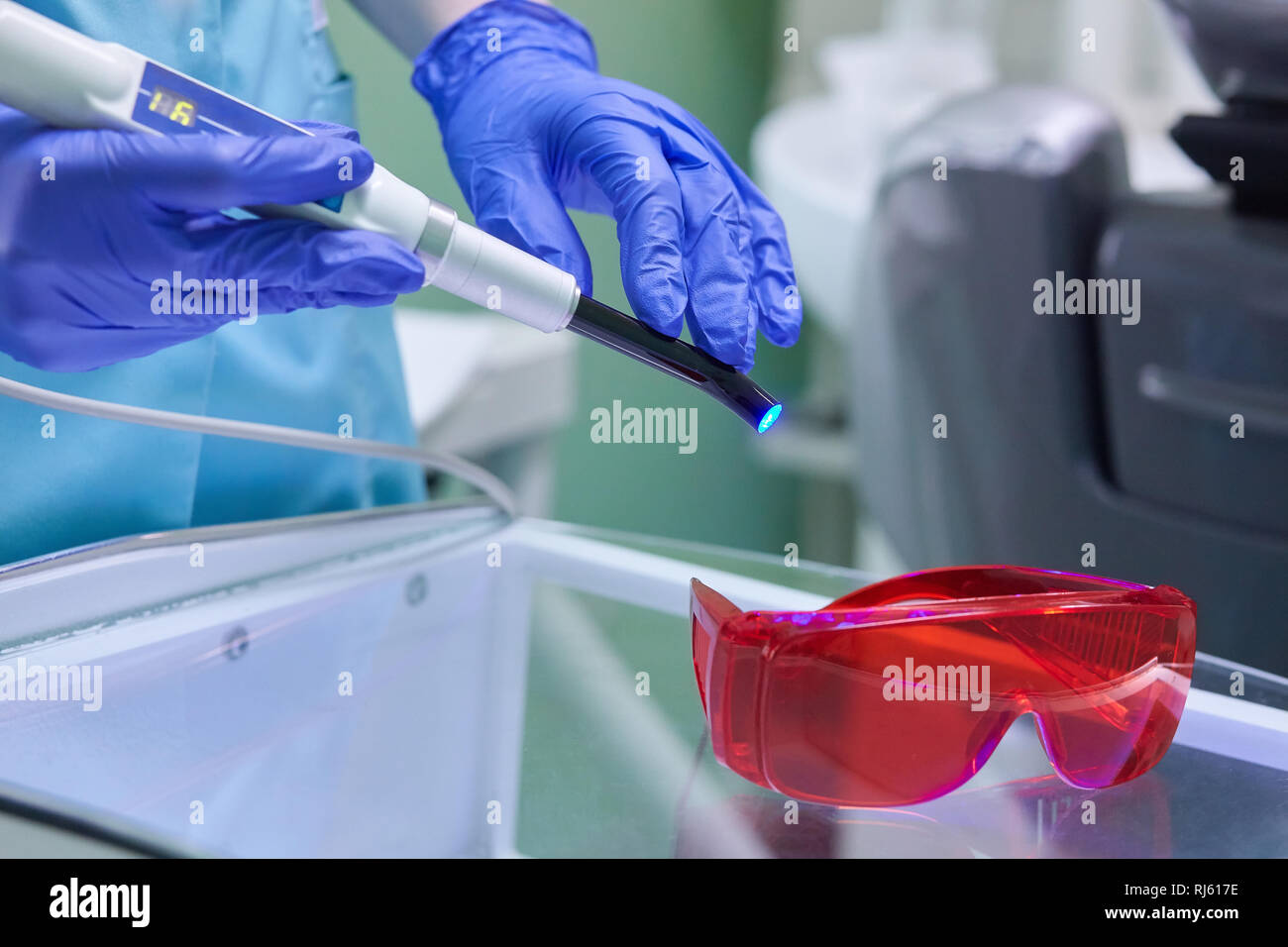 Mano nel guanto medicale azienda Dental indurimento ai raggi UV della luce. Di polimerizzazione a ultravioletti con lampada rossa occhiali di bloccaggio Foto Stock